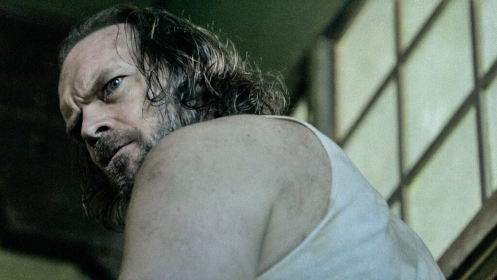 Frame grab from Penance Lane Teaser trailer of Tyler Mane looking over his shoulder in a creepy environment
