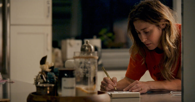 Frame grab from Earthquake Note of Kat Foster in a medium shot writing on a notepad