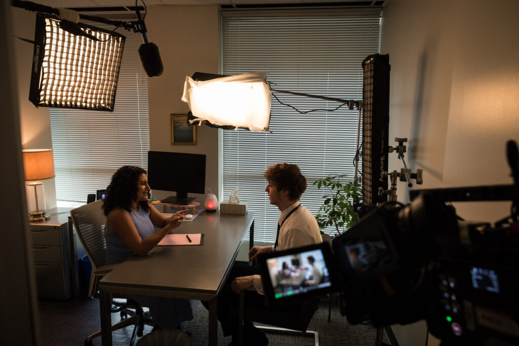 camera equipment fills a small office with two people seated in conversation